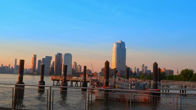 New York City skyline from waterfront ferry pier, steel railings and mooring piles frame the East River.