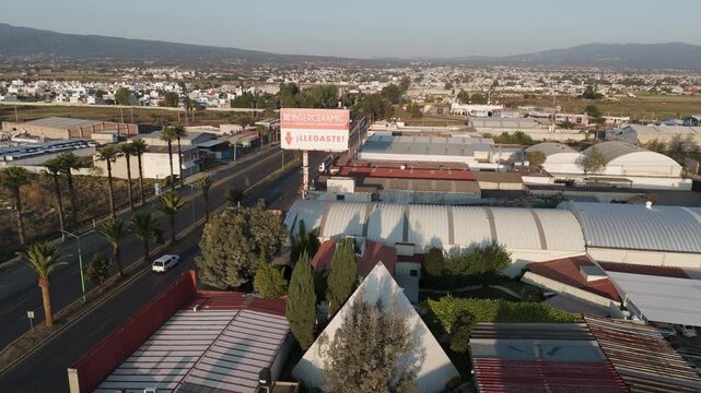 atlixco, puebla, mexico - 04.20.2026: Beautiful aerial establishing shot of the city, revealing the urban landscape with warehouses, a highway, and distant mountains under a clear sky at sunset