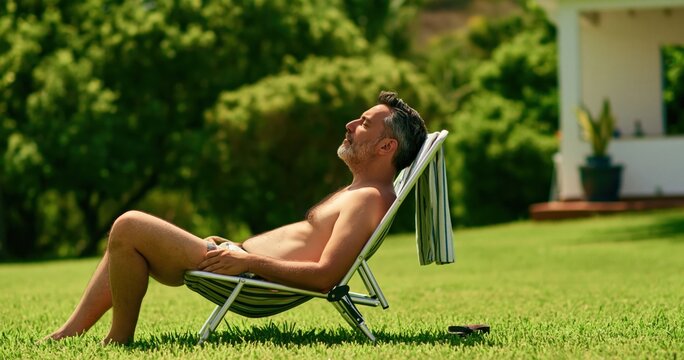 Man relaxing on a chair in the backyard as a mature male sunbathing in the garden