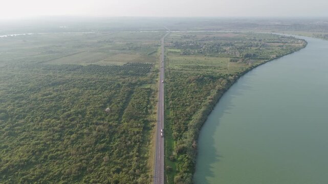 Aerial perspective of a straight highway running between a vast green forest and the serene waters of a wide river, showcasing the intersection of nature and human infrastructure in Tuxpan Mexico