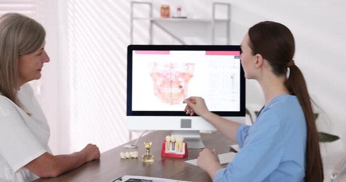 Doctor consulting woman regarding dental implantation at desk in clinic,
