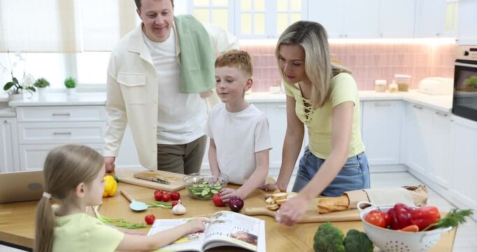 Parents and their kids making salad at wooden table in kitchen, camera moving in