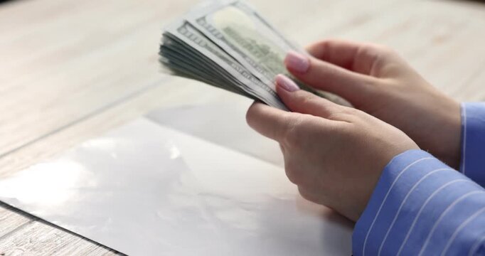 Bonus. Woman opening envelope with dollar banknotes at color wooden table, closeup