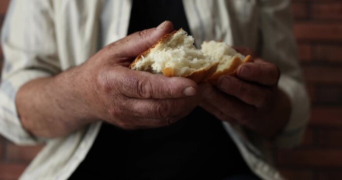 Poverty. Homeless senior man breaking piece of bread indoors, closeup. Camera moving forward