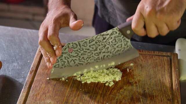 Chef chopping garlic with a damascus steel cleaver