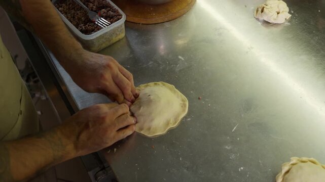 Tattooed chef's hands making traditional empanadas