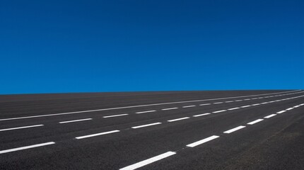 Fototapeta premium Empty Asphalt Road with White Lines Under a Clear Blue Sky