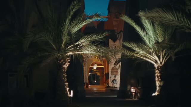 Lit palm trees framing traditional Moroccan riad archway entrance at night