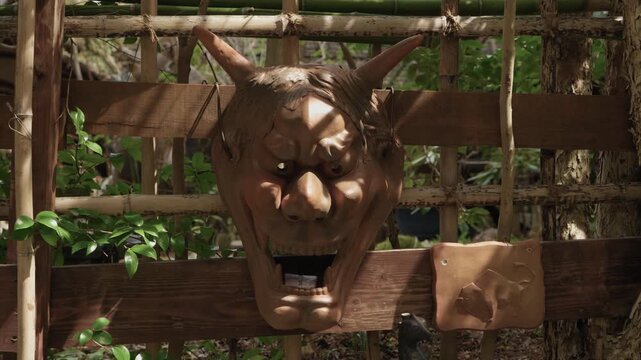 Wooden Oni demon mask with horns mounted on bamboo fence in garden Kyoto Japan