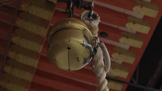 Golden suzu prayer bell with woven rope hanging at Shinto shrine in Japan
