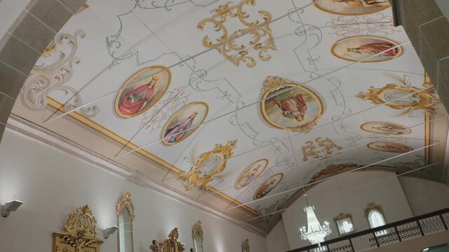 Ornate church ceiling with painted saints medallions gold scrollwork and chandelier