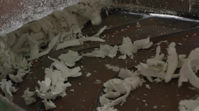 White plastic flakes moving along conveyor from grinder for regrinding into pellets