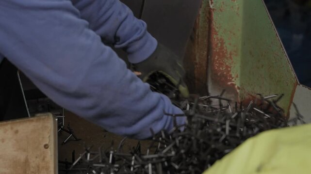 Gloved worker hands feeding tangled plastic mold scrap into grinder at recycling plant