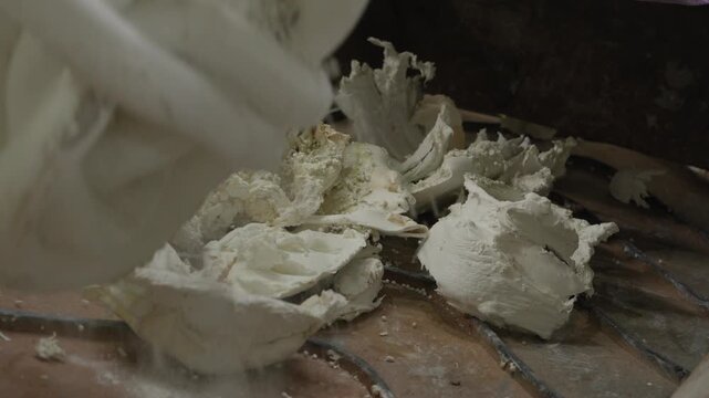 Crushed white polyurethane foam chunks resting on rusty metal grate at recycling plant