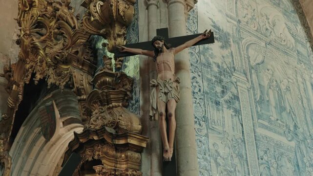 Wooden crucified Christ figure against blue azulejo tile wall and gilded carving in church