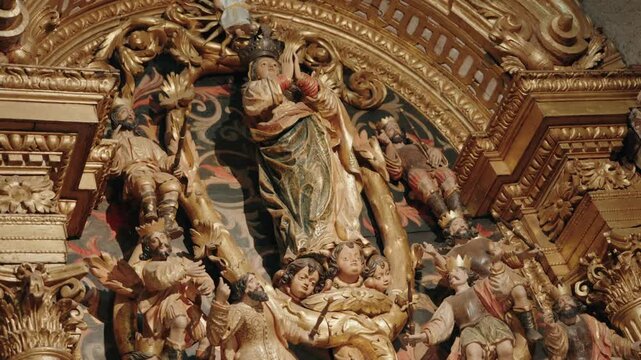 Painted wood sculptures of crowned figure surrounded by angels and saints in gilded retable