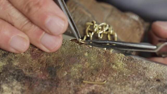 Jeweler hands using tweezers to assemble gold chain links on workbench close up