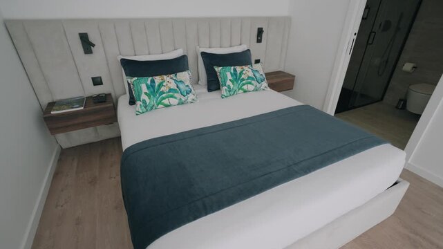 Clean modern bedroom with white double bed teal throw cushions and wood nightstands
