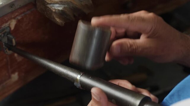 Jeweler hammering gold ring on steel mandrel with mallet to shape it close up in workshop