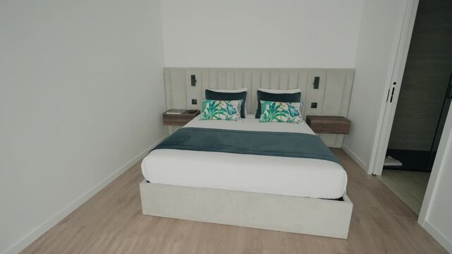 Bright modern bedroom with white double bed teal throw cushions wood floor and nightstands