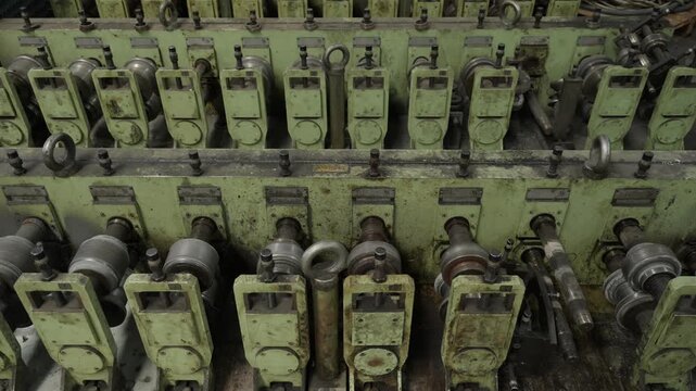 Rows of weathered green cast metal machine parts with shafts and bearings in factory