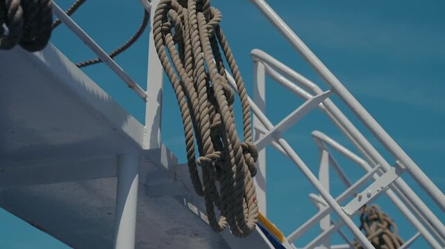 Thick mooring rope looped over white metal handrail of ship deck under clear blue sky