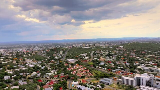 Drone view of Windhoek city spreading across the valley beneath a dramatic cloudy sky. The capital city spreads across a wide valley ringed by rugged highland mountains under an open sky.