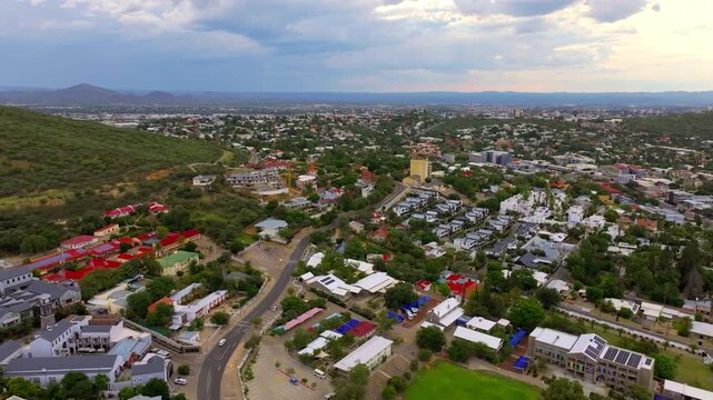 High aerial of Windhoek's residential and commercial districts stretching toward distant mountain ranges. A sprawling capital ringed by highland mountains.