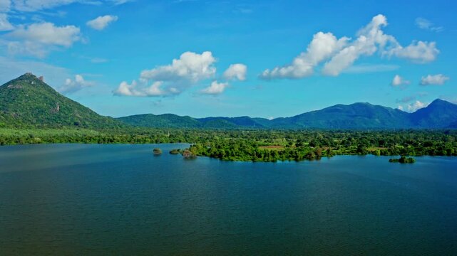 Aerial view over a large lake dotted with small green islands, surrounded by farmland and rolling hills under a bright tropical sky.