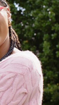 Vertical video: Panning woman turning, laughing toward camera in park with pink sweater, red shades