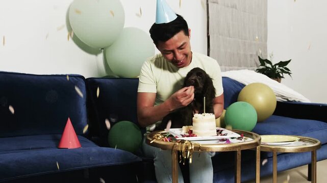 Man wearing cone hat reaching toward candle, breaking cake and feeding dog during celebration