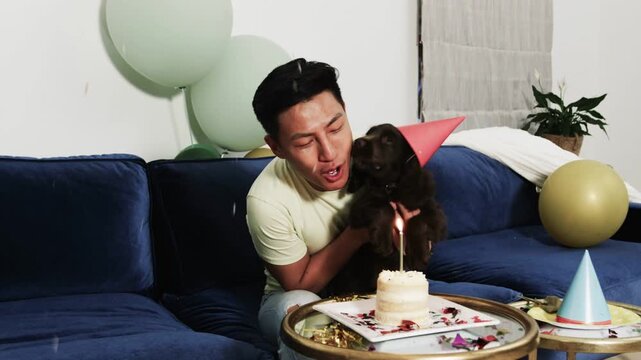 Seeing lit candle, man holding dog, placing hat and leaning to blow candle for marketing
