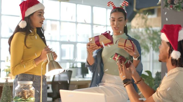 Center woman checking gifts and giving one as left woman reaching, man accepting at office holiday
