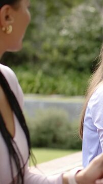 Vertical video: Laughing woman in lilac top reacting after left friend gesturing at bench, watch