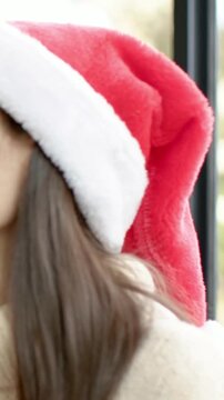 Vertical video: Smiling woman in Santa-hat sweater turning as friend entering holding mug by window