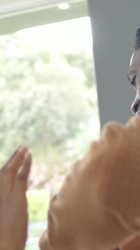 Vertical video: Checking watch man in brown sweatshirt gesturing and laughing by window during chat
