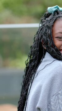 Vertical video: Seeing camera, smiling child turning in park, gray sweater and teal bow, copy space
