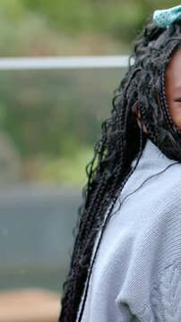 Vertical video: Smiling girl turning toward camera on balcony by railing, gray sweater, copy space