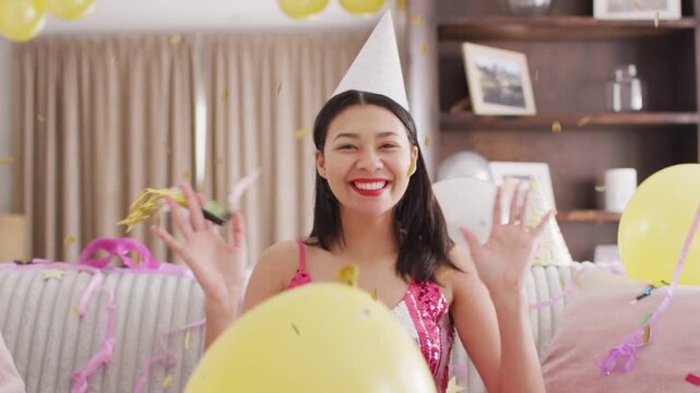 Woman sitting, confetti falling, causing cheering and waving, yellow balloon hiding torso, partying