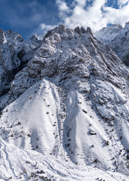 Aerial view of the snow-covered Hushe Valley mountains with rugged peaks, steep slopes, and scattered trees under a blue sky in Khaplu, Gilgit Baltistan, Pakistan.