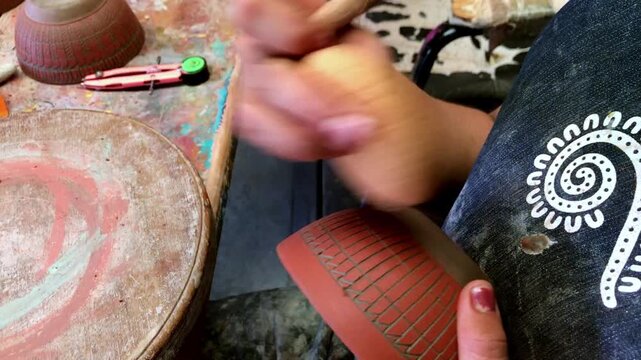 Close up of artisan decorating handmade clay bowl with carved traditional pattern before firing. Skilled pottery craftsmanship showcasing ceramic artistry and cultural heritage