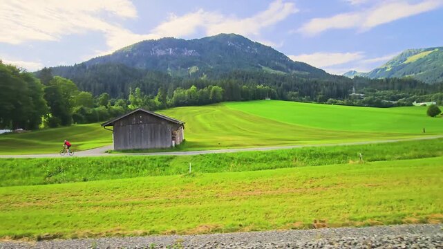 Austria train journey past open fields, scattered farm buildings, pine forests, and mountain hillsides, capturing peaceful countryside scenery from the window.