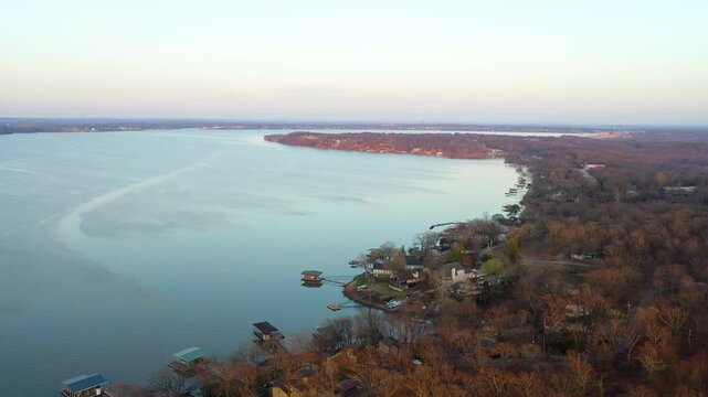 Drone aerial near Branson, Missouri, showing calm lake water, waterfront homes, covered docks, wooded shoreline, and a peaceful residential cove in soft evening light.