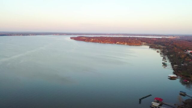 High aerial above a Branson, Missouri lakeside neighborhood, capturing calm water, lakefront houses, wooded shoreline, and private boat docks along a tranquil cove.