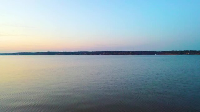 Drone shot near Branson, Missouri, looking across a wide Ozark lake with calm water, tree-covered shoreline, distant houses, and soft evening colors in the sky.