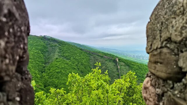 A scenic view of lush green hills observed through an ancient stone wall opening.