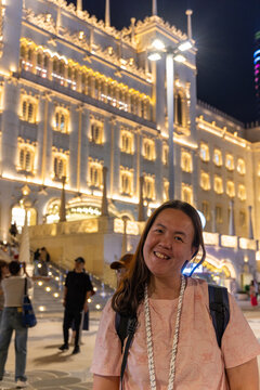 Tourist smiling in front of the illuminated facade of the Lijun Pangdu Plaza in Zhuhai, China, at night