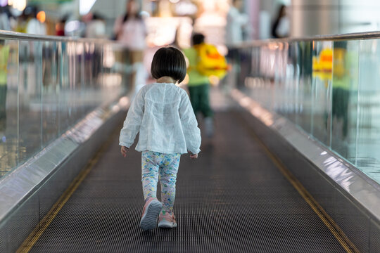 Little girl running on moving walkway in airport terminal