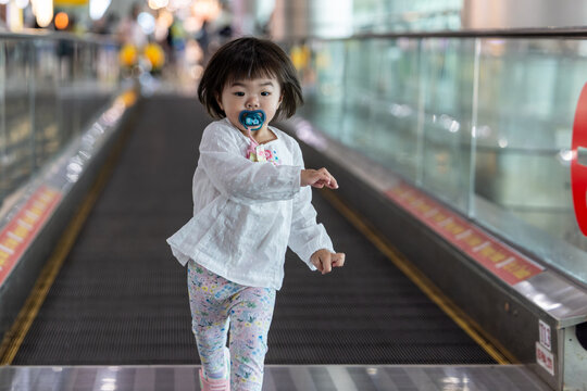 Little girl running on moving walkway in airport terminal