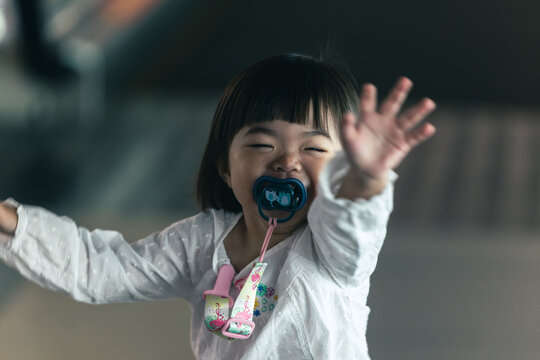 Happy baby girl waving and smiling with pacifier